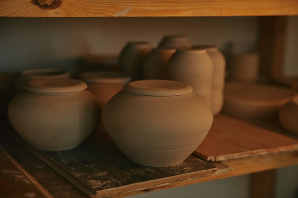 close up view of ceramic bowls and dishes on wooden shelves at pottery studio - Foto, Imagem