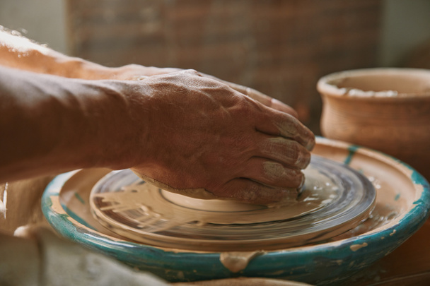 selective focus of male potter hands working on pottery wheel at workshop - Fotó, kép