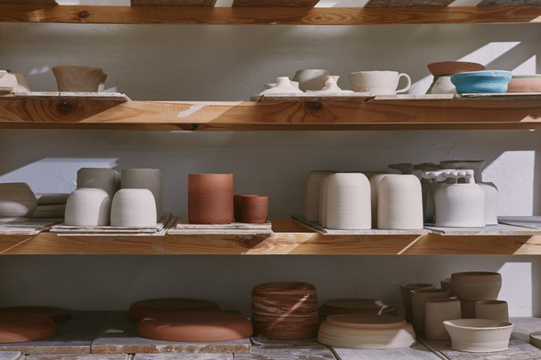 керамические чаши и посуда на деревянных полках в мастерской керамики
 - Фото, изображение