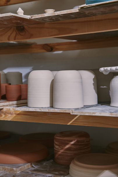 foco selectivo de cuencos y platos de cerámica en estantes de madera en el estudio de cerámica
 - Foto, imagen