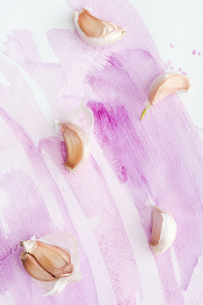 top view of delicious raw garlic on white surface with pink watercolor strokes - Foto, Imagem