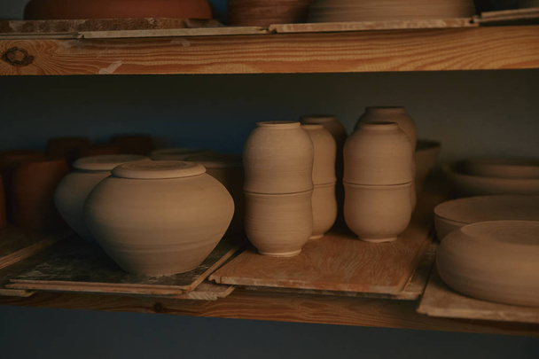 κεραμικά κύπελλα και πιάτα πάνω σε ξύλινα ράφια στο εργαστήριο κεραμικής - Φωτογραφία, εικόνα