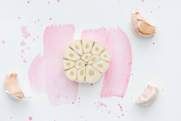 vista superior del ajo picante especiado en la superficie blanca con trazos de acuarela rosa
 - Foto, Imagen