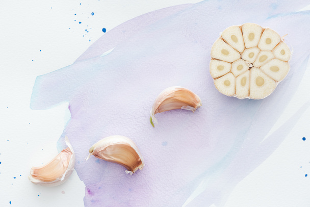 top view of uncooked sliced garlic on white surface with purple watercolor strokes - Фото, изображение