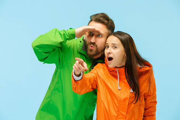 La joven pareja sorprendida posando en el estudio en chaquetas de otoño aisladas en azul
 - Foto, Imagen