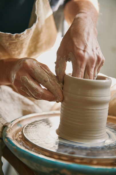 enfoque selectivo de las manos del hombre trabajando en la rueda de cerámica en el taller
 - Foto, Imagen