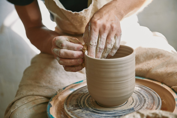 imagen recortada del artesano masculino que trabaja en la rueda de alfarería en el estudio de cerámica
 - Foto, imagen