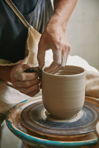 gedeeltelijke weergave van mannelijke werkman werkt op potters wiel op aardewerk studio - Foto, afbeelding