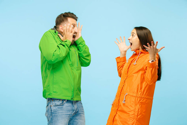 The young surprised couplel posing at studio in autumn jackets isolated on blue - Foto, Imagen