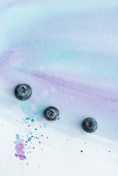 Draufsicht auf frische Blaubeeren auf weißer Oberfläche mit violetten Aquarellstrichen und Flecken - Foto, Bild