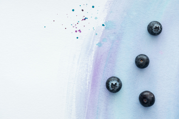 top view of delicious ripe blueberries on white surface with purple watercolor strokes - Fotoğraf, Görsel