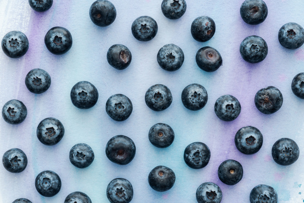 top view of ripe blueberries on white surface with purple watercolor strokes - Fotoğraf, Görsel