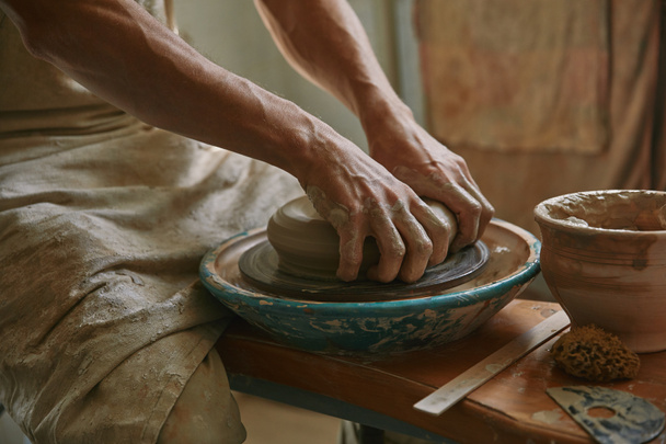 abgeschnittenes Bild eines männlichen Handwerkers, der im Töpferatelier an der Töpferscheibe arbeitet - Foto, Bild