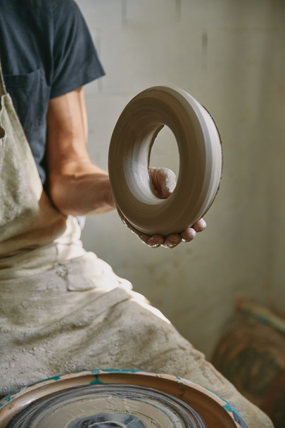 обрізане зображення професійного гончаря в фартусі, що тримає глину в керамічній студії
 - Фото, зображення