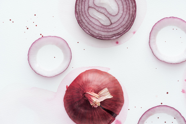 Draufsicht auf geschnittene würzige rote Zwiebel auf weißer Oberfläche mit rosa Aquarellfleck - Foto, Bild
