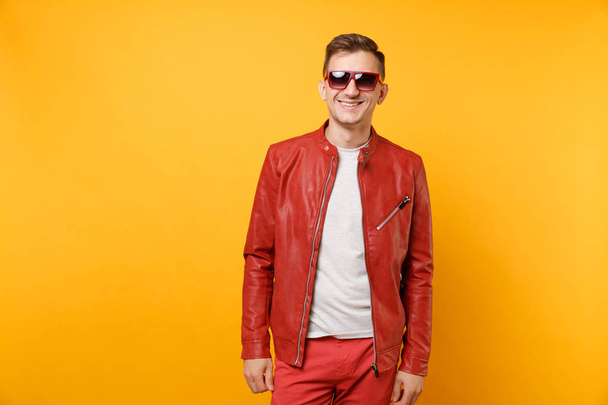 Portrait vogue cute handsome young man 25-30 years in red leather jacket, t-shirt sunglasses isolated on bright trending yellow background. People sincere emotions lifestyle concept. Advertising area - Foto, afbeelding
