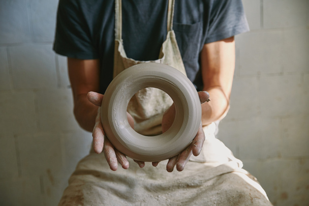 enfoque selectivo de alfarero profesional en delantal que sostiene la arcilla en el estudio de cerámica
 - Foto, imagen