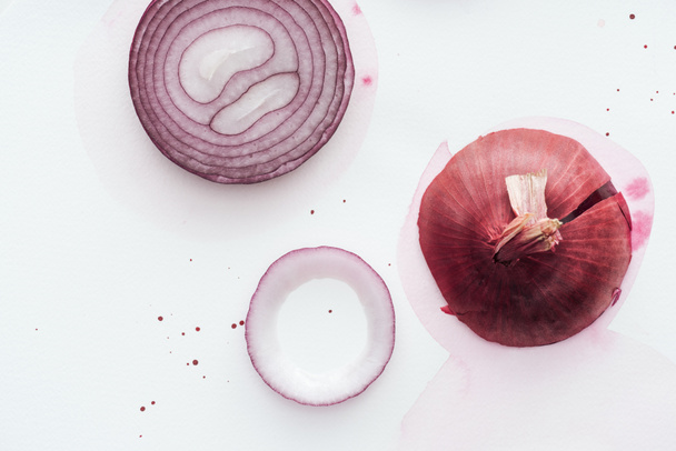 top view of raw whole red onion with slice on white surface with pink watercolor blots - Foto, imagen
