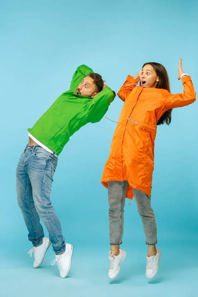 The young surprised couplel posing at studio in autumn jackets isolated on blue - Fotoğraf, Görsel