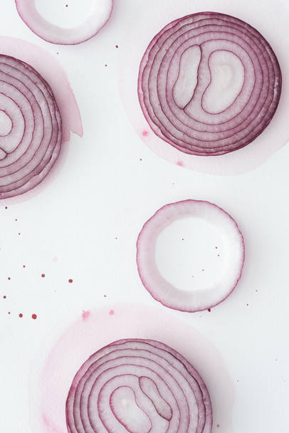 top view of raw slices of red onion on white surface with pink watercolor blots - Φωτογραφία, εικόνα
