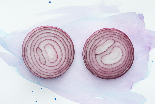 top view of two slices of red onion on white surface with purple watercolor strokes - Foto, imagen