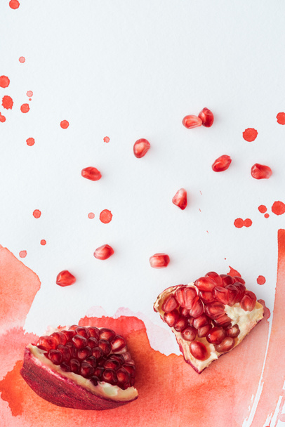 Draufsicht auf köstlichen Granatapfel auf weißer Oberfläche mit roten Aquarellstrichen - Foto, Bild