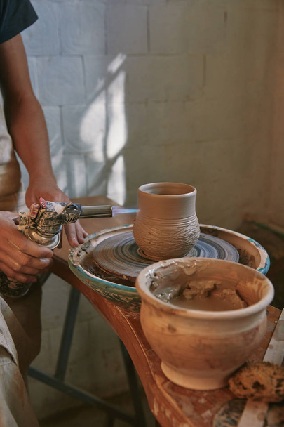 częściowy widok mężczyzna Pottera w fartuch wypalania gliny garnek w pracowni ceramiki - Zdjęcie, obraz