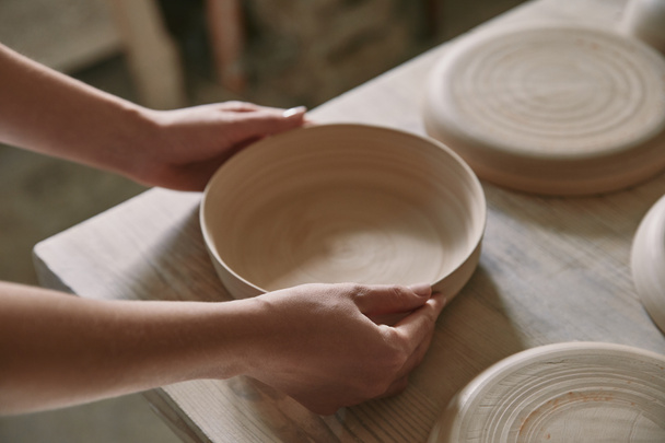 vista parcial de la mujer poniendo plato de cerámica en la mesa en el taller
 - Foto, Imagen