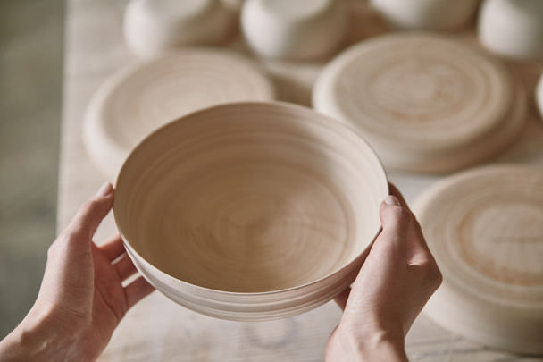 imagem cortada de mulher segurando prato de cerâmica no estúdio de cerâmica
  - Foto, Imagem