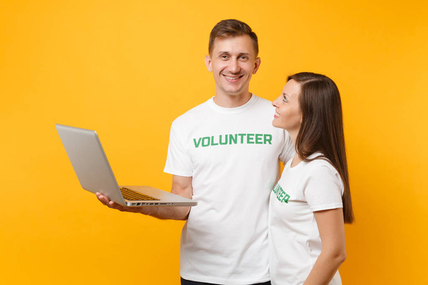 Kollegat pari valkoinen t-paita kirjoitus vihreä vapaaehtoinen käyttäen kirjoittamalla kannettavan tietokoneen tietokoneen eristetty keltaisella pohjalla. Vapaaehtoinen vapaa työ, apu apu, hyväntekeväisyys armon tiimityö käsite
 - Valokuva, kuva