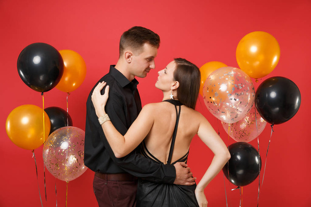 A divatos fiatal pár fekete ruhában ünneplése születésnapi ünnepi buliba elszigetelt világos piros háttérben levegő léggömbök. St. Valentin nemzetközi női nap boldog új évet 2019 fogalom. Mintája fel - Fotó, kép