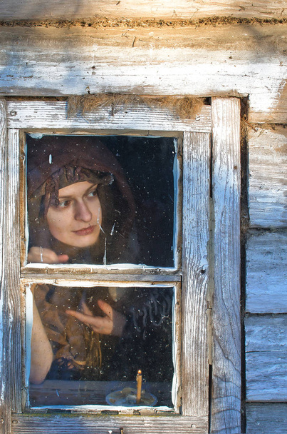 красивая крестьянка, завернутая в шерстяную шаль с коварной улыбкой смотрит в окно дома, что-то, что ей было интересно
 - Фото, изображение