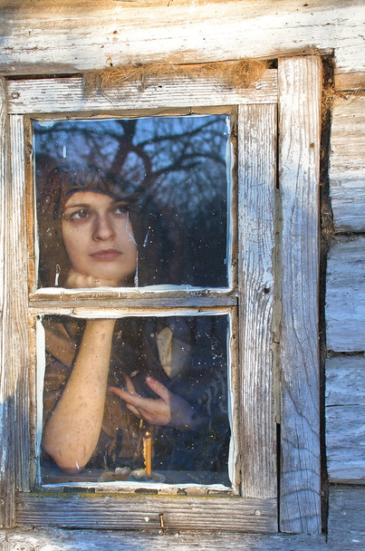 χωρική συγκρατείται το κεφάλι της με το χέρι της και κοίταξε έξω από το παράθυρο το χειμώνα ξεθώριασμα ημέρα - Φωτογραφία, εικόνα