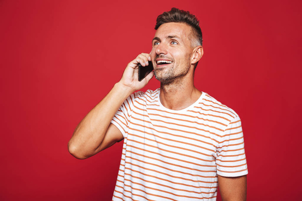 Portrait of a happy man standing over red background, talking on mobile phone - Foto, Imagem