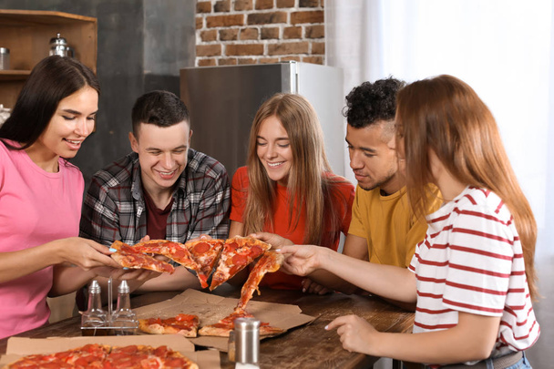 Jonge mensen plezier op feestje met heerlijke pizza binnenshuis - Foto, afbeelding