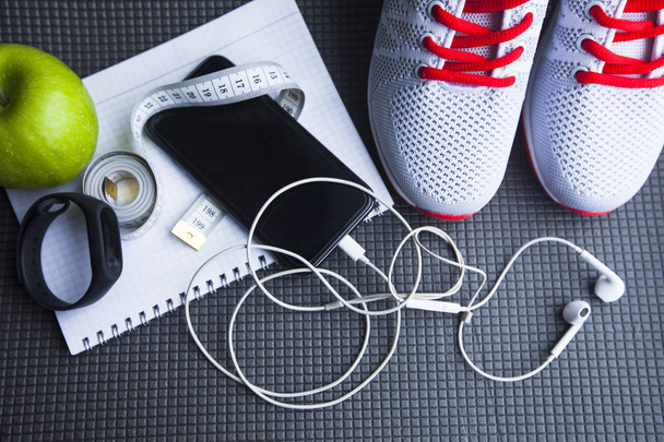 Time for diet slimming weight loss concept. Sport fitness, apple, sneakers, bottle of water and yellow weights on grey rubber background - Foto, Imagem