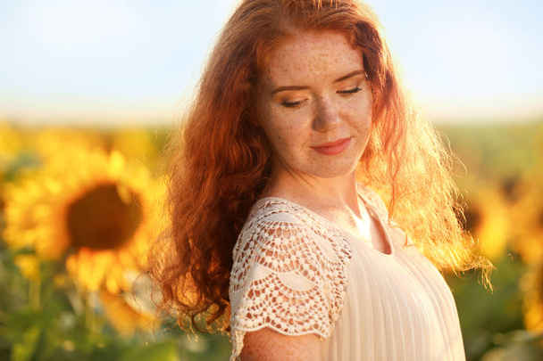 Gyönyörű vörös hajú nő, napraforgó mező napsütéses napon - Fotó, kép