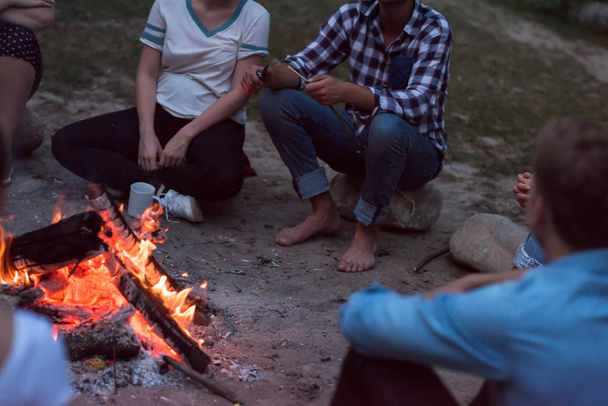 group of happy young friends relaxing and enjoying summer evening around campfire - 写真・画像