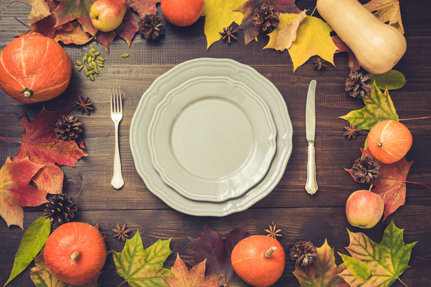Autumn and Thanksgiving day table setting with fallen leaves, pumpkins, spices, grey plate and vintage cutlery on brown wooden table. Top view, toned image. - Fotografie, Obrázek