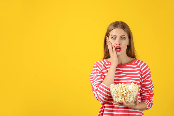 Emotional young woman with bowl of popcorn on color background - Fotoğraf, Görsel