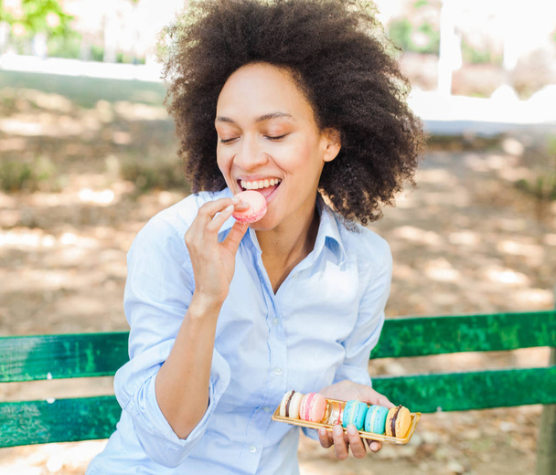Feliz jovem afro-americano mulher comer macarons biscoito no parque
 - Foto, Imagem