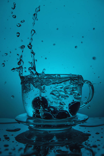 Splash of water in a cup on a blue background. - Photo, Image
