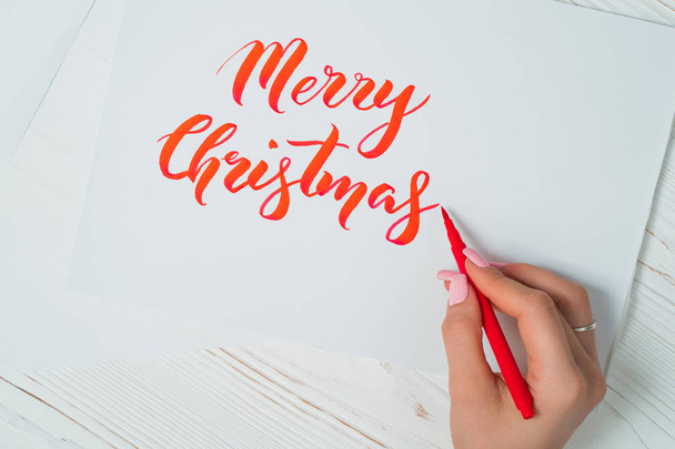 Merry Christmas congratulations. Calligrapher writes with red ink on white card. Calligraphy. Ornament font. The art of lettering. Graphic design, handwriting, creation concept. - Photo, image