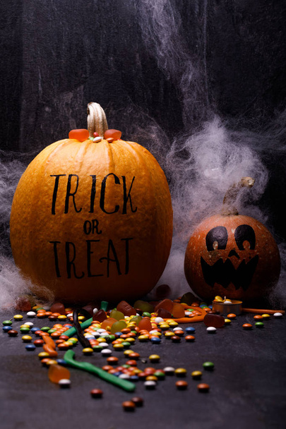 Halloween pumpkins with sweet candies on dark background. Concept of autumn holidays, close-up. Lettering trick or treat on gourd. - Foto, Imagem