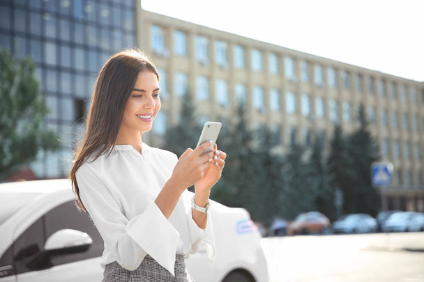 Jonge zakenvrouw met mobiele telefoon in de buurt van auto - Foto, afbeelding