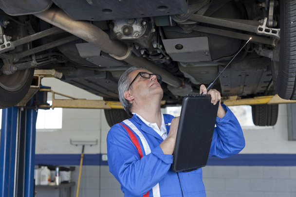 Mechanic scrutinizing the car and writing down something on clipboard - 写真・画像