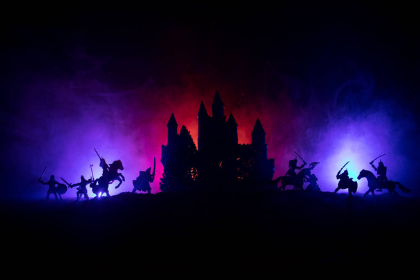Средневековая боевая сцена с кавалерией и пехотой. Силуэты фигур как отдельные объекты, борьба между воинами на темном, тонированном туманном фоне со средневековым замком. Селективный фокус - Фото, изображение