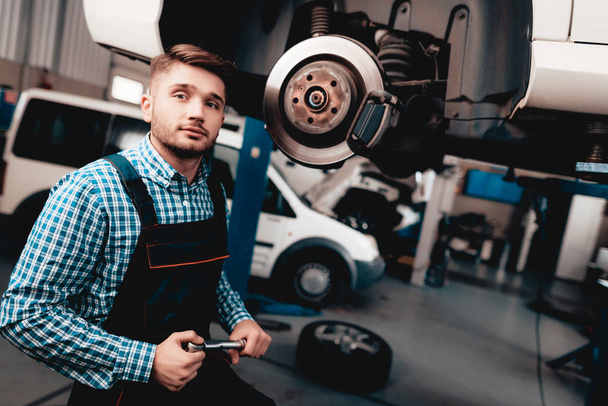 Young Auto Mechanic Repairs Automotive Hub In Garage. Professional Uniform. Service Station Concept. Confident Engineer Stare. Detail Repairing. Under The Vehicle. Automobile Diagnostic. - Zdjęcie, obraz