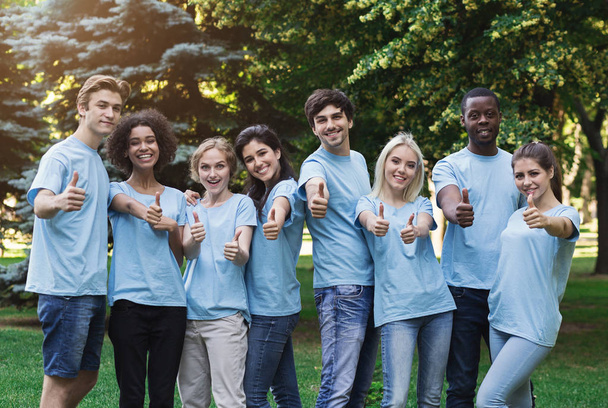 Pewni Młodzi wolontariusze kciuki skrzyżowane się w parku - Zdjęcie, obraz