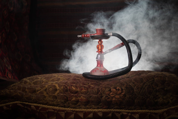 Hookah hot coals on shisha bowl making clouds of steam at Arabian interior. Oriental ornament on the carpet. Stylish oriental shisha with backlight. For Shisha advertisement. Selective focus - Photo, Image